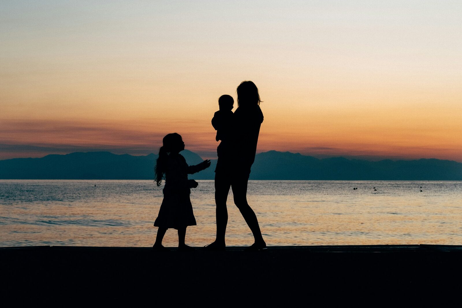 Silueta de madre con dos niños al atardecer junto al mar