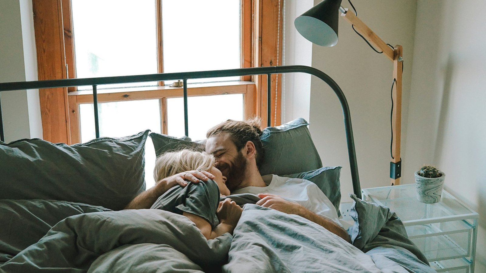 Manos entrelazadas de una pareja sobre una cama con luz suave